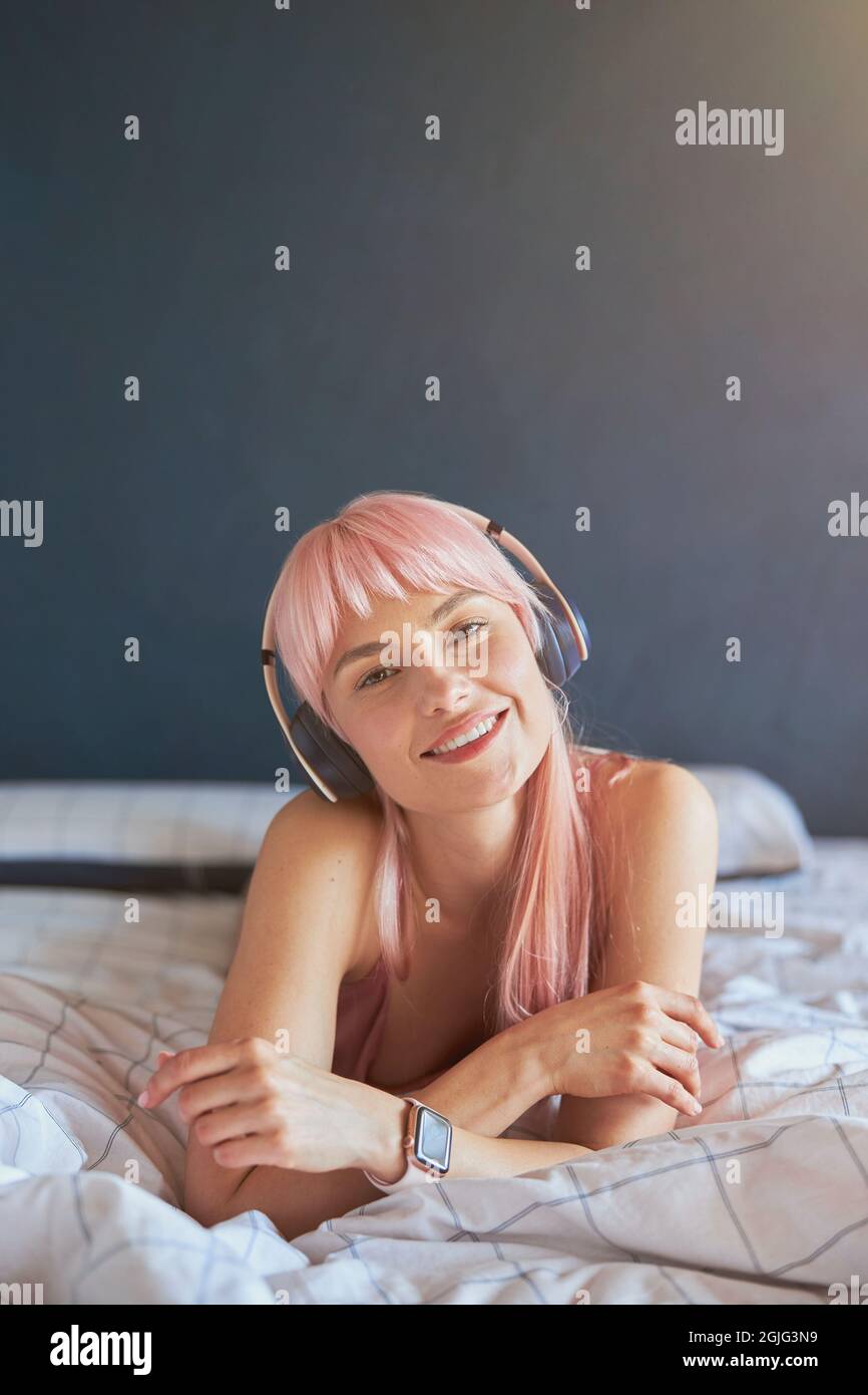 Portrait de beau modèle avec cheveux roses écoutant de la musique sur un lit confortable à la maison Banque D'Images