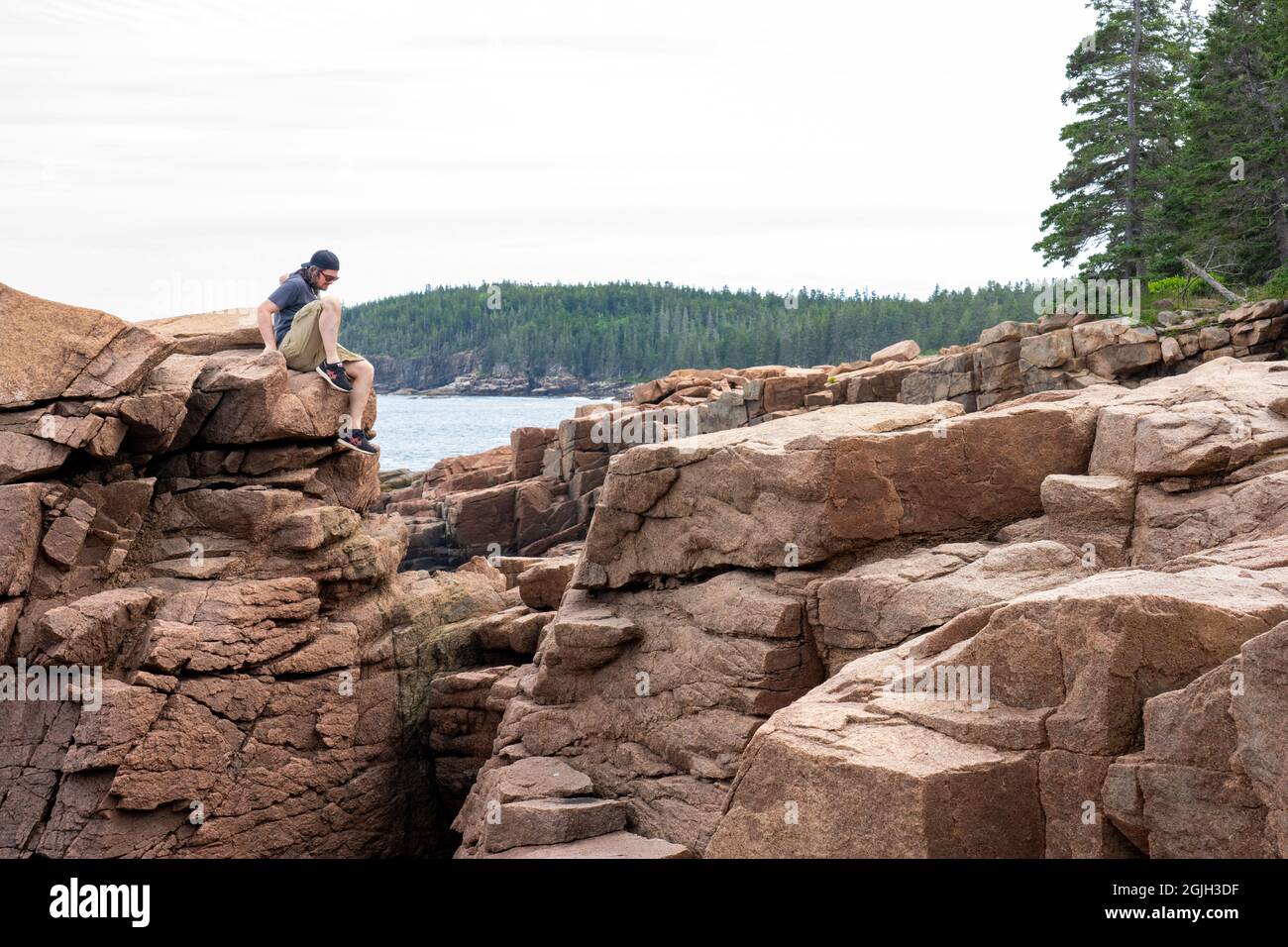 Parc national Acadia, Maine, États-Unis. Homme grimpant prudemment sur la falaise près de Thunder Hole. Banque D'Images