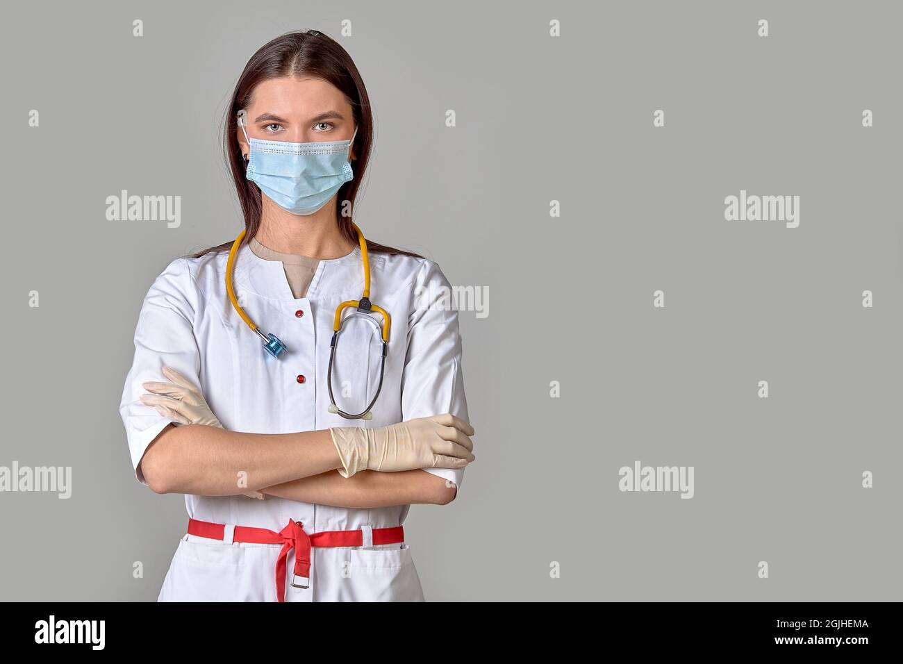 Une jeune femme médecin sous un manteau blanc avec un stéthoscope et un masque médical sur un fond gris isolé. Copier l'espace Banque D'Images