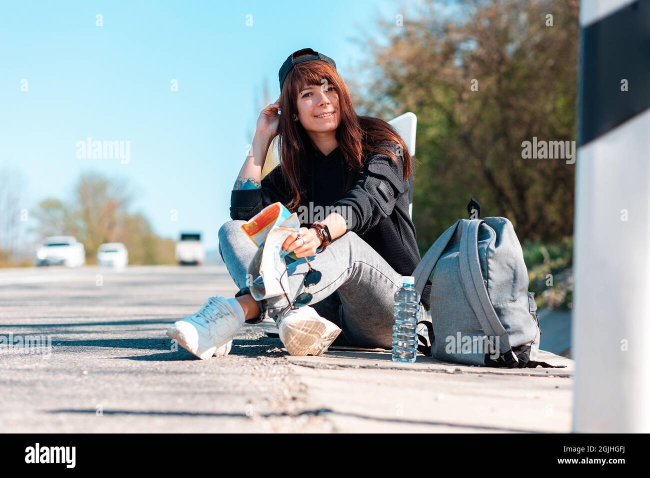 Concept de randonnée et de voyage local. Une femme hipster en casquette  avec des mains à embout de tatouage assis le long de la route et lisant une  carte papier Photo Stock -