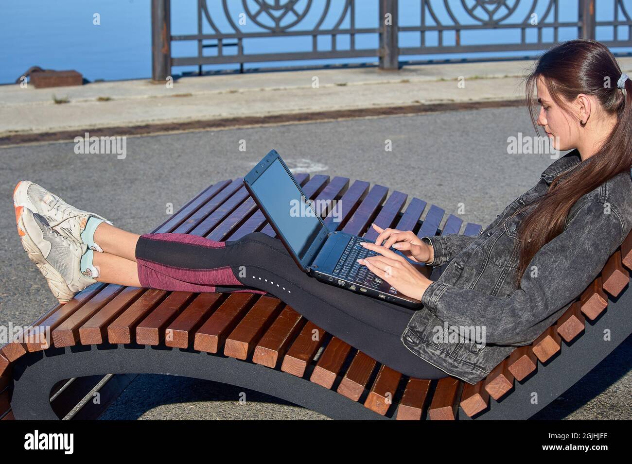 Jeune femme assise sur un banc avec un ordinateur portable et travaillant un jour d'été ensoleillé Banque D'Images