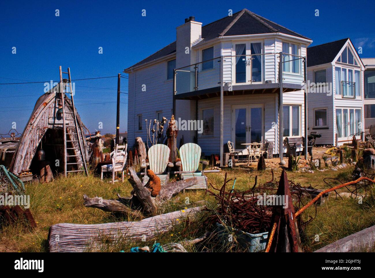 Une charmante maison de plage en bois blanc à Camber Sands, son jardin rustique décoré de façon unique avec du bois flotté, un bateau renversé. Banque D'Images