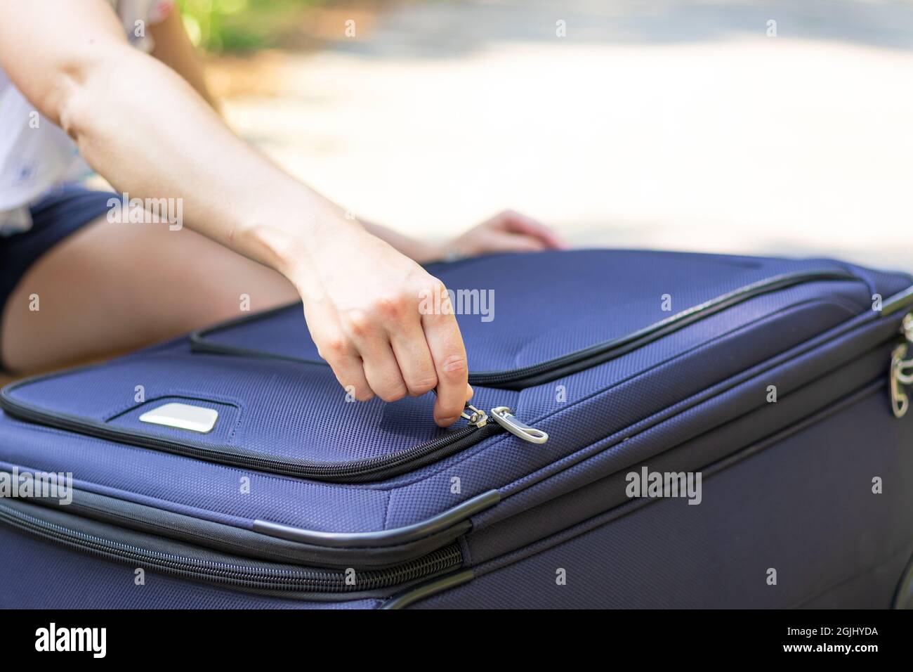 Les mains des femmes ouvrent une valise avec des choses sur une route de forêt par une journée ensoleillée d'été. Gros plan. Mise au point sélective Banque D'Images