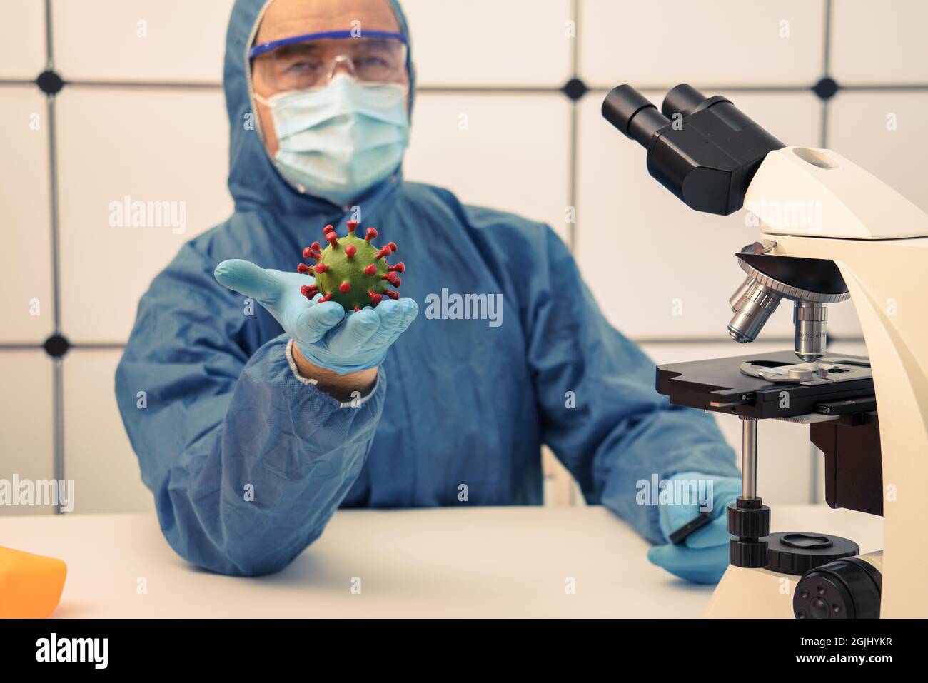 Médecin avec un modèle de coronavirus en main dans un bureau médical avec un microscope Banque D'Images