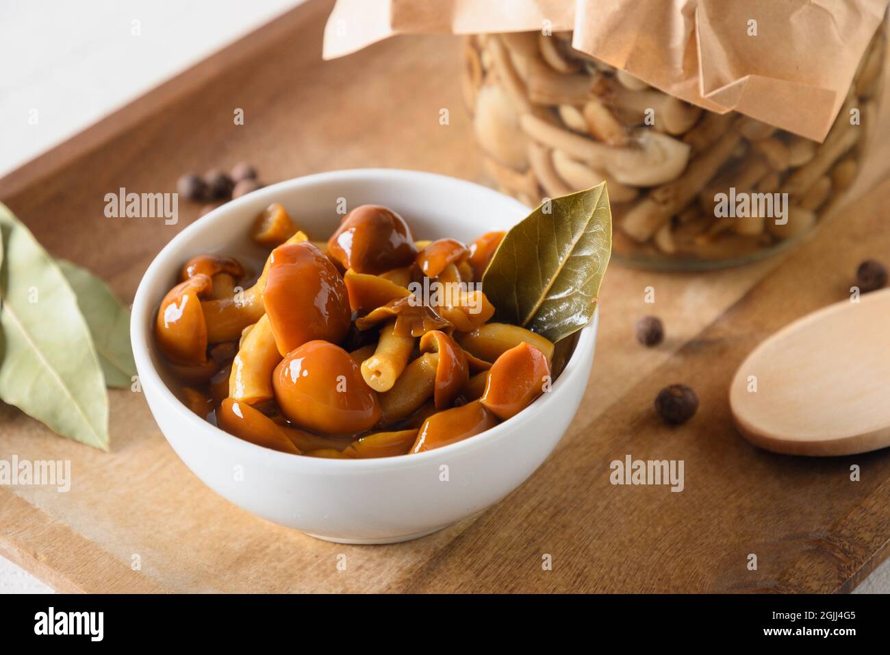 Champignons au miel marinés servis dans un bol avec feuilles de Laurier et épices sur fond blanc. Gros plan. Banque D'Images