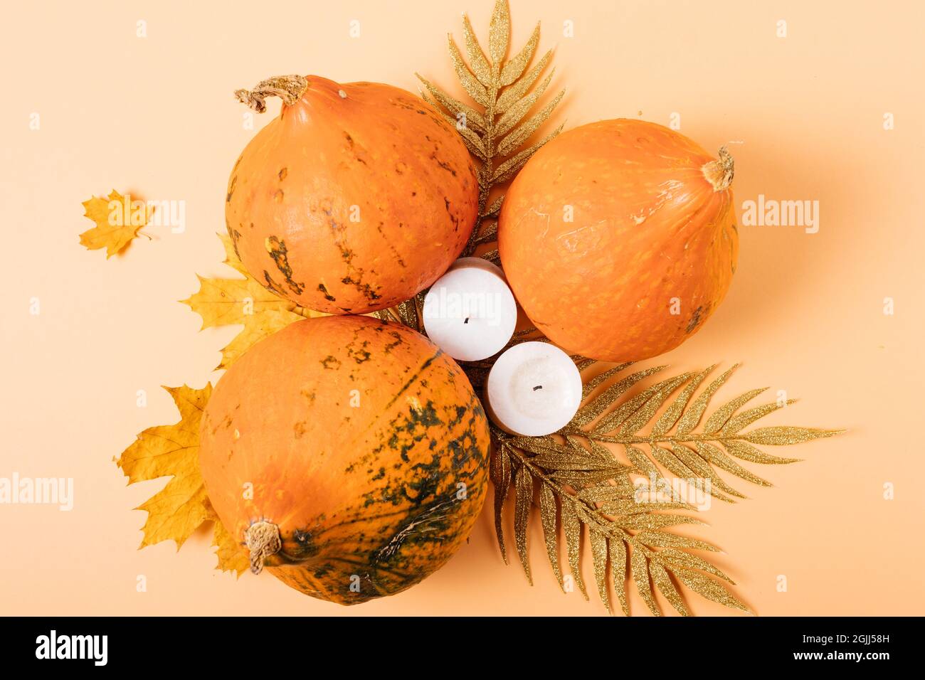 Décoration festive d'automne avec citrouilles, bougies et feuilles dorées sur fond orange, plat. Banque D'Images