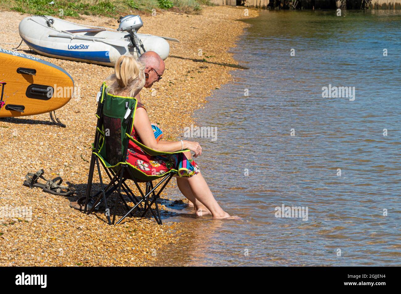 Couple assis dans des chaises sur la plage pagayant leurs pieds dans la mer un jour chaud de septembre, Angleterre, Royaume-Uni Banque D'Images