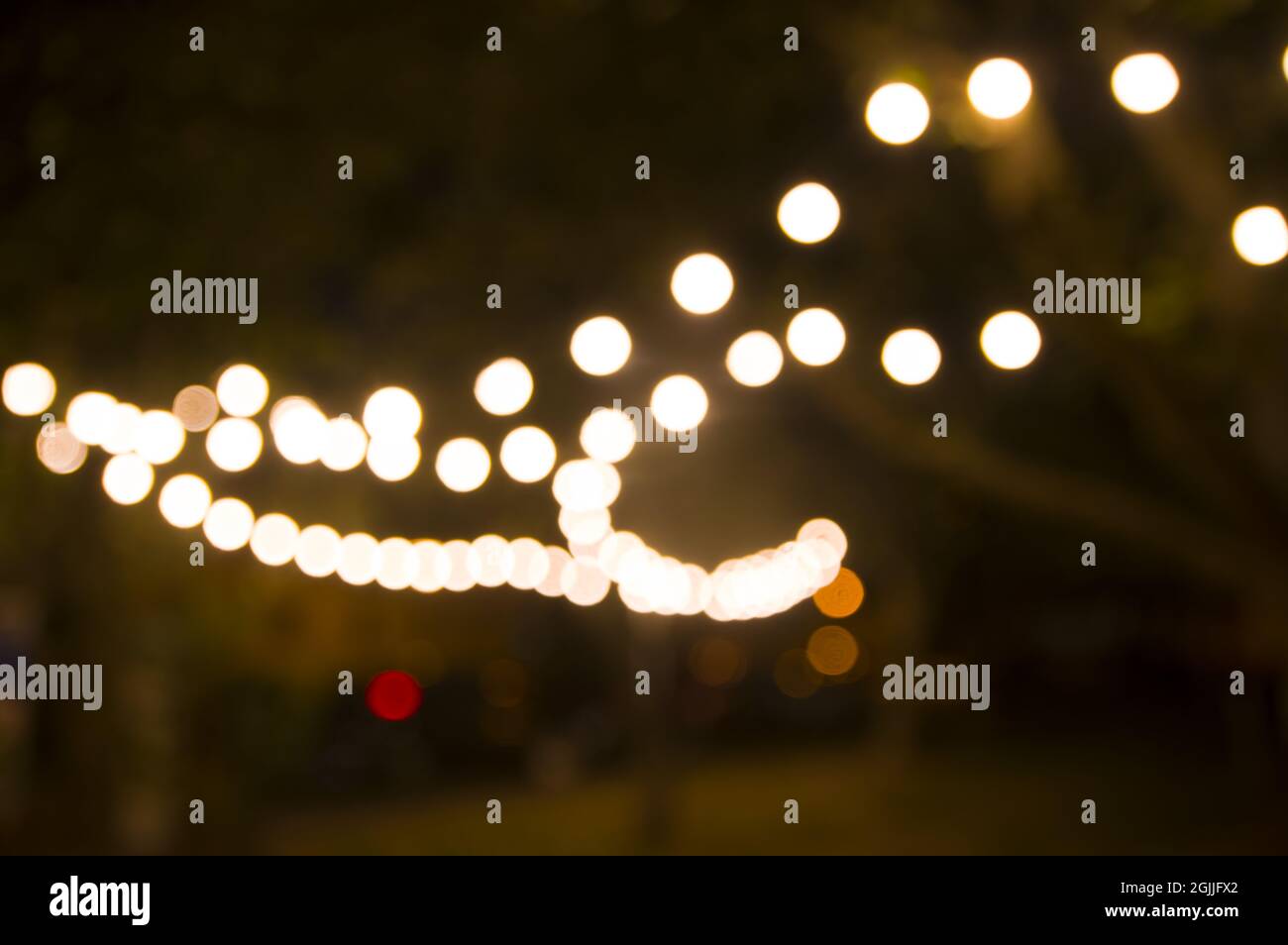 Arrière-plan abstrait flou, éclairage de l'arrière-cour, lumière dans le jardin du soir, guirlande électrique défocuée. Guirlande lumineuse d'ampoules sur les arbres illuminant la scène nocturne Banque D'Images