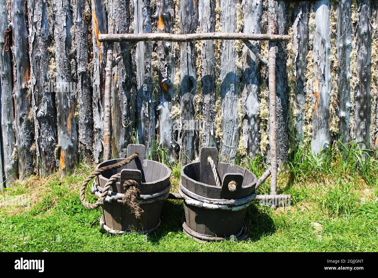 Seaux à eau en bois à l'ancienne avec un cadre de transport, dans l'herbe par un mur de bois. Banque D'Images