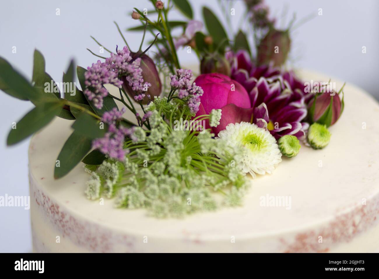 Hochzeitsträume - Un gros plan d'un gâteau de mariage rustique orné de fleurs délicates et de verdure, présentant un design simple mais élégant. Banque D'Images