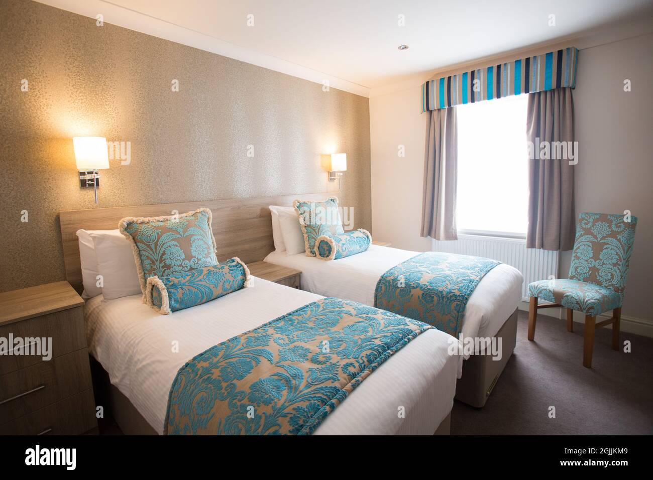 Chambre d'hôtel simple avec deux lits simples, coussins turquoise et chaise  Photo Stock - Alamy