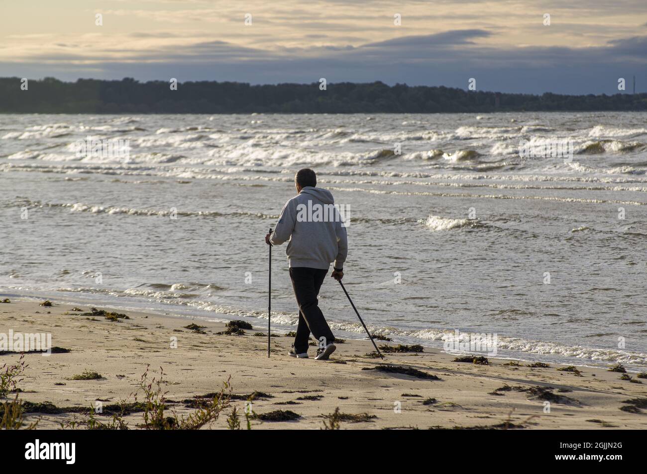 Vieil homme faisant des exercices cardio et musclés à l'extérieur. Un mode de vie actif et sain. Marche nordique, entraînement sur une plage de sable en bord de mer en soirée Banque D'Images