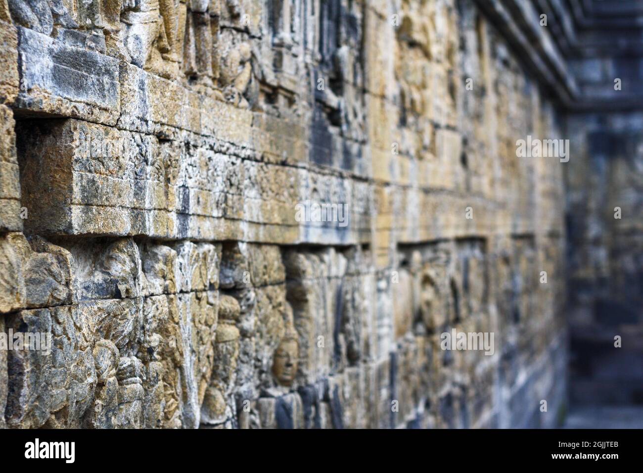 Intérieur de l'ancien temple Borobudur terrasses inférieures. Gros plan de bas reliefs en pierre sur le mur dans un couloir avec arrière-plan bokeh. Personne. Banque D'Images