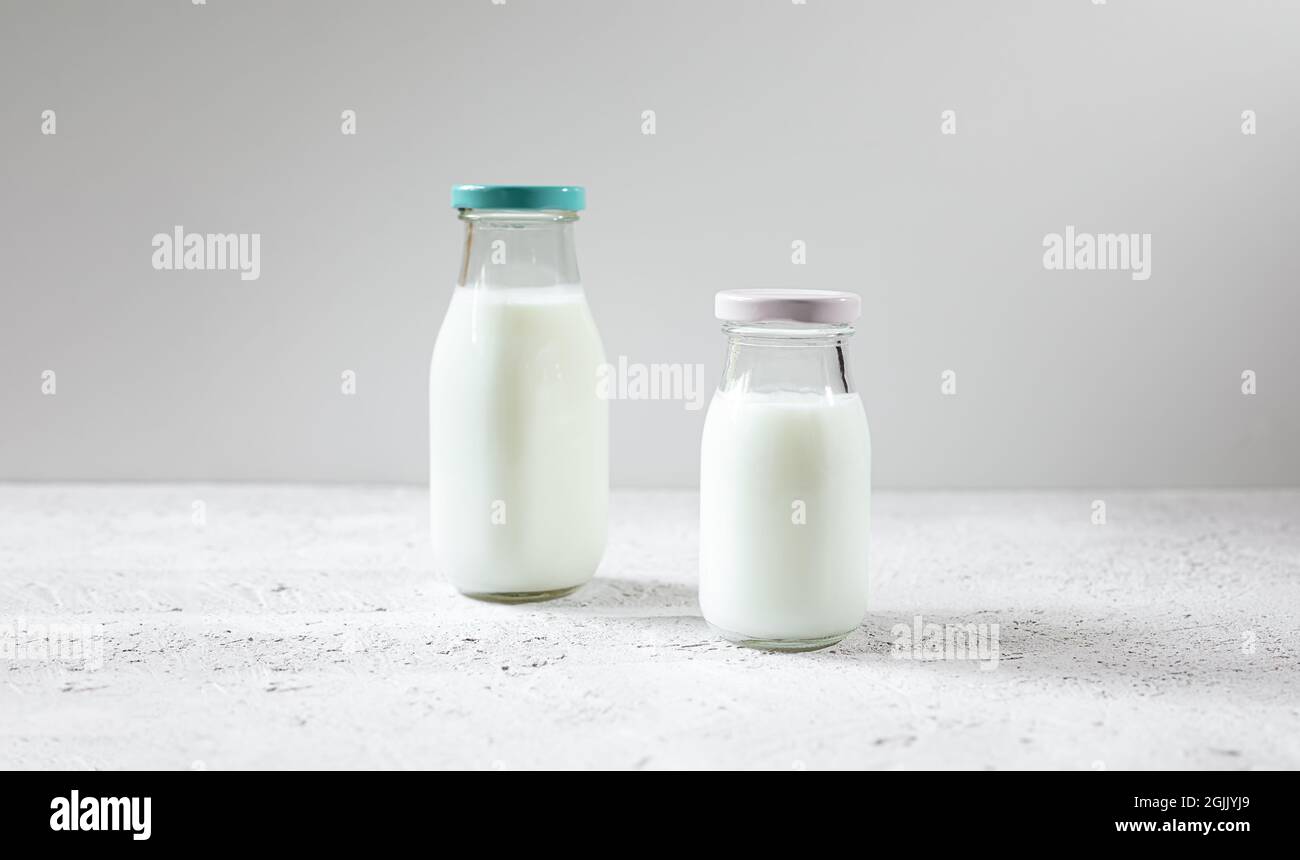Deux bouteilles en verre réutilisables de lait biologique frais ou de produits laitiers sur une table en bois blanc Banque D'Images