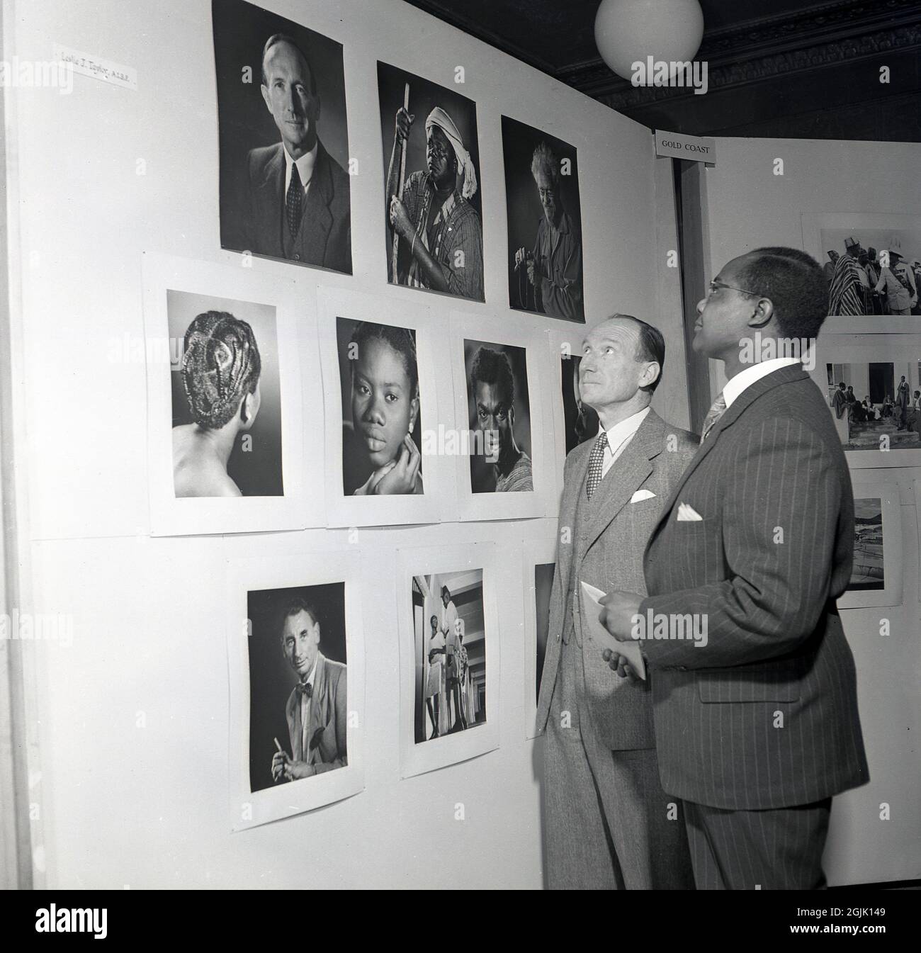 Années 1950, historique, lors d'une exposition de photos, deux hommes en costume debout regardant des portraits d'Afrique et de la Gold Coast, pris par le photographe Leslle J. Taylor, AIBP, Londres, Angleterre, Royaume-Uni. Banque D'Images