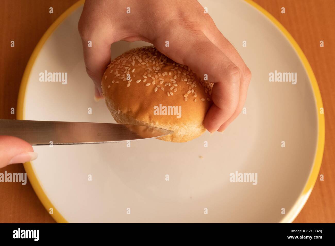 Une femme coupe un hamburger de graines de sésame avec un couteau coupé à moitié prêt Banque D'Images