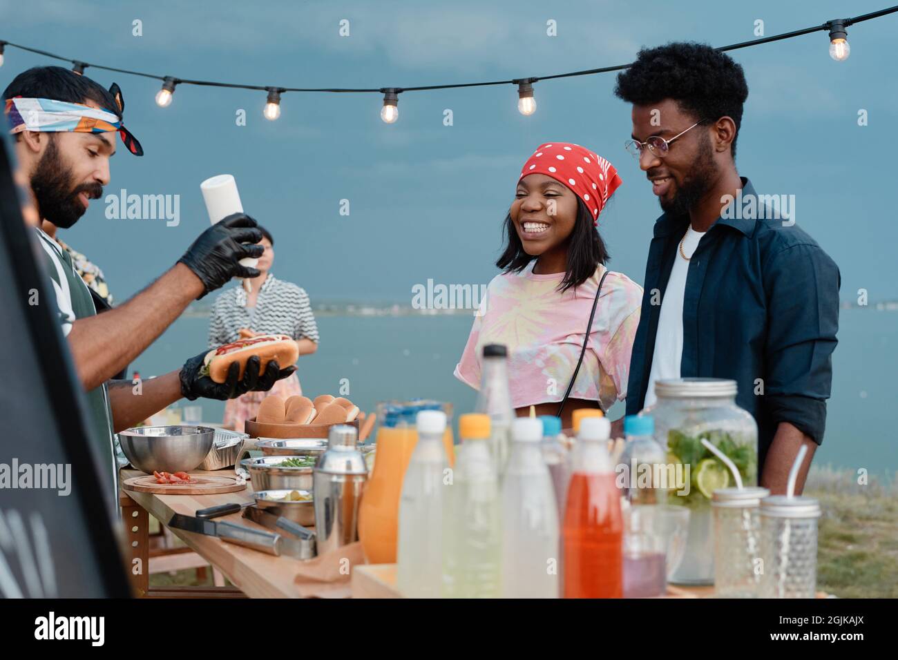 Jeunes couples africains à l'écoute du processus de préparation des hot-dogs qu'ils ont déjeuner sur la plage à l'extérieur Banque D'Images