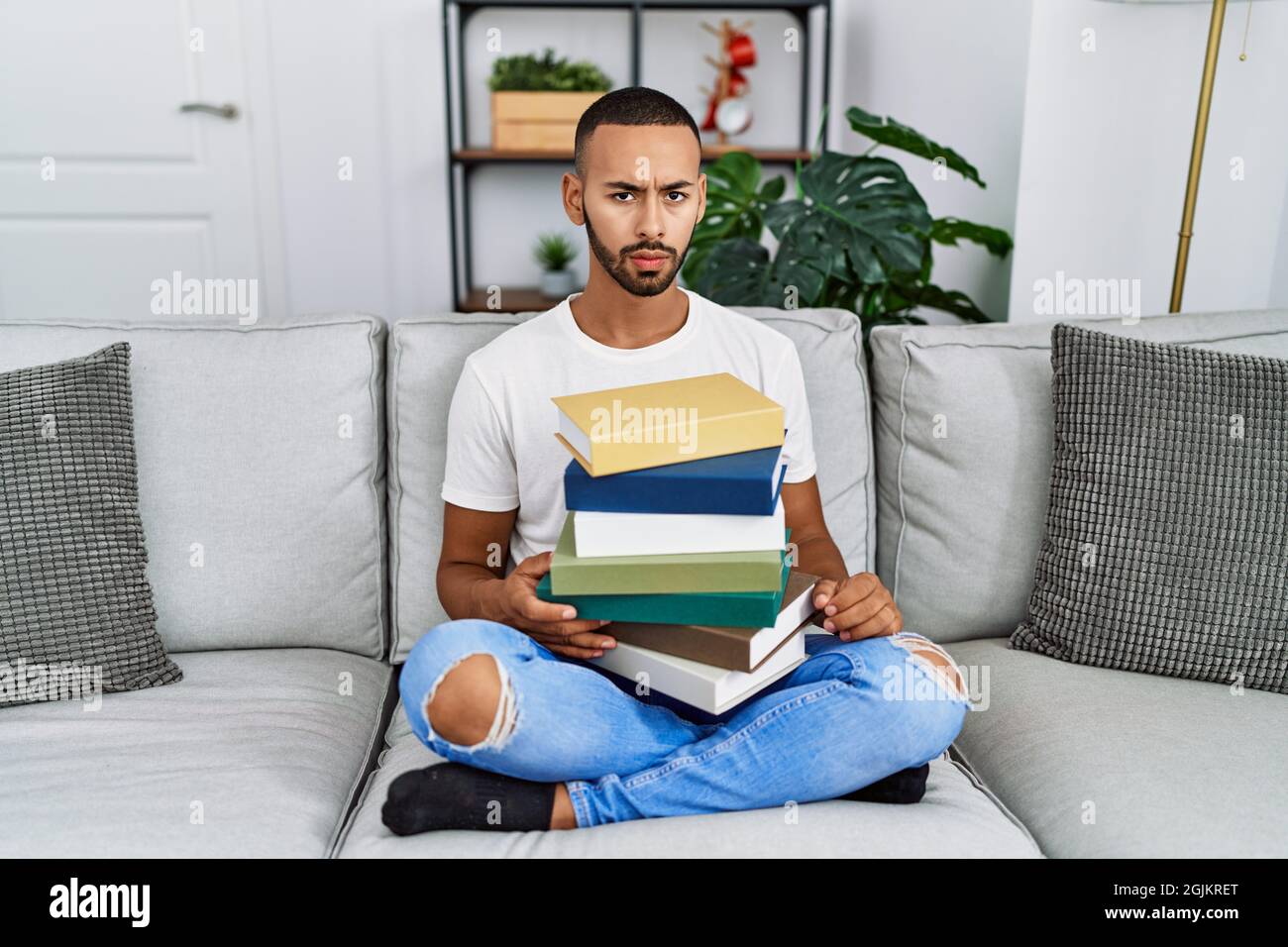 Un jeune Afro-américain tenant une pile de livres assis sur le canapé ...