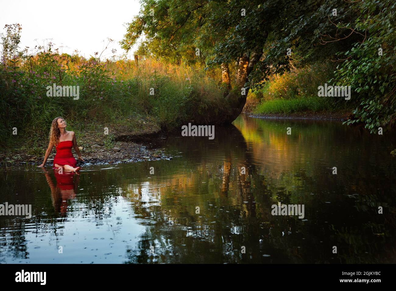 Une belle fille dans une robe rouge près d'une rivière Banque D'Images