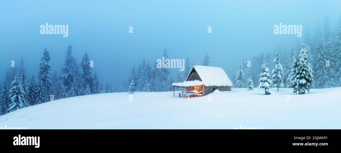 Panorama fantastique sur le paysage d'hiver avec cabine en bois dans une forêt enneigée. Maison confortable dans les montagnes de Carpathian. Concept de vacances de Noël Banque D'Images