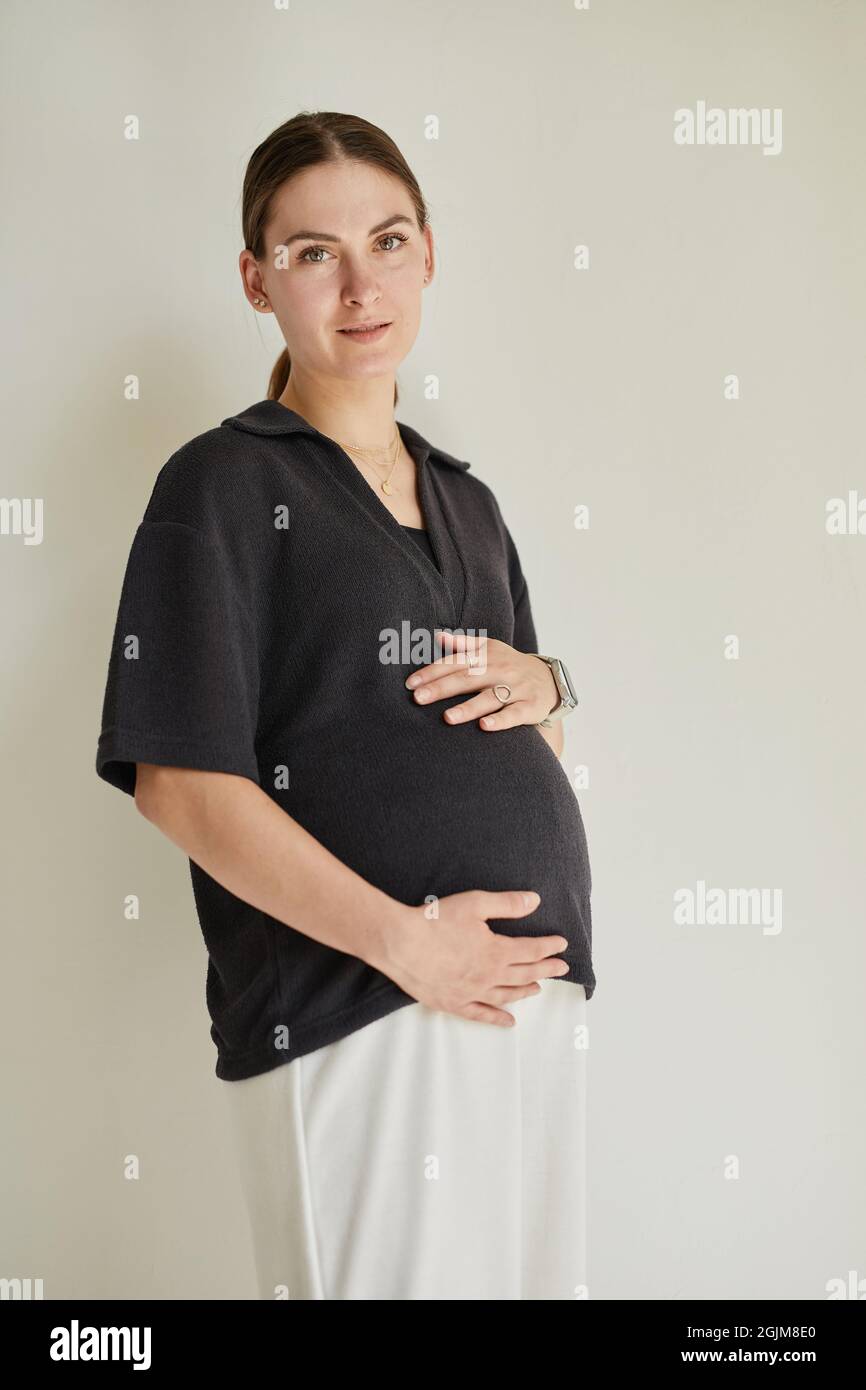 Portrait de contenu attrayante enceinte d'âge moyen Femme caucasienne en noir et blanc confortable porter le ventre contre un arrière-plan isolé Banque D'Images