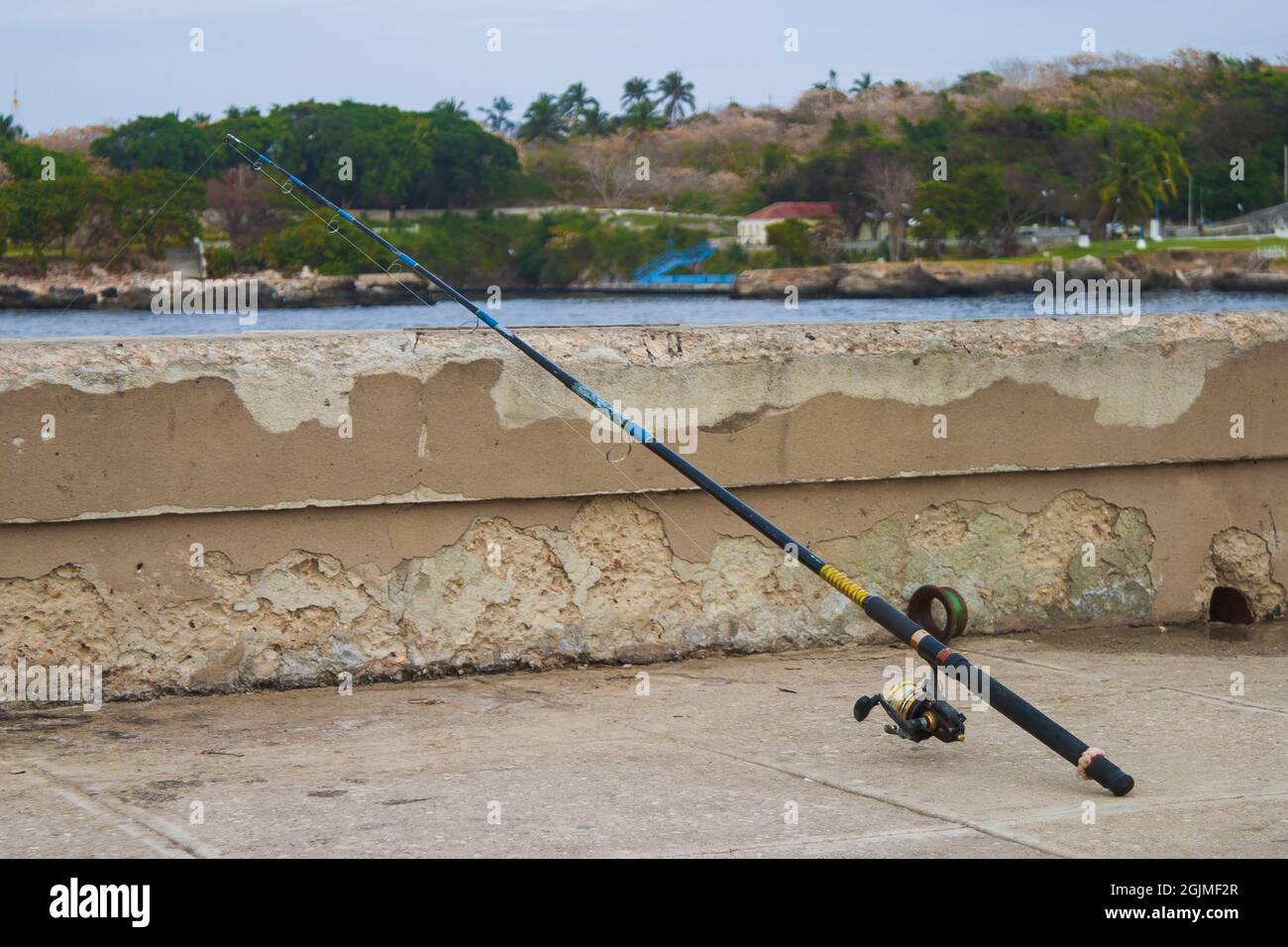Canne à pêche sur une barrière de chemin en béton à côté d'une rivière Banque D'Images