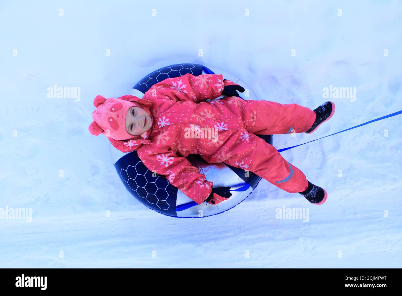 Une fille dans une combinaison d'hiver est assise sur un tubing. L'enfant glisse dans la neige. Banque D'Images