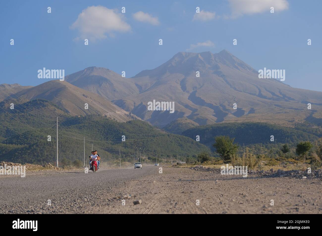 Aksaray.Turquie.Une Audi blanche et un homme sur moto conduite sur route sale avec nuage de poussière derrière elle et magnifique et immense montagne de Hasan Banque D'Images