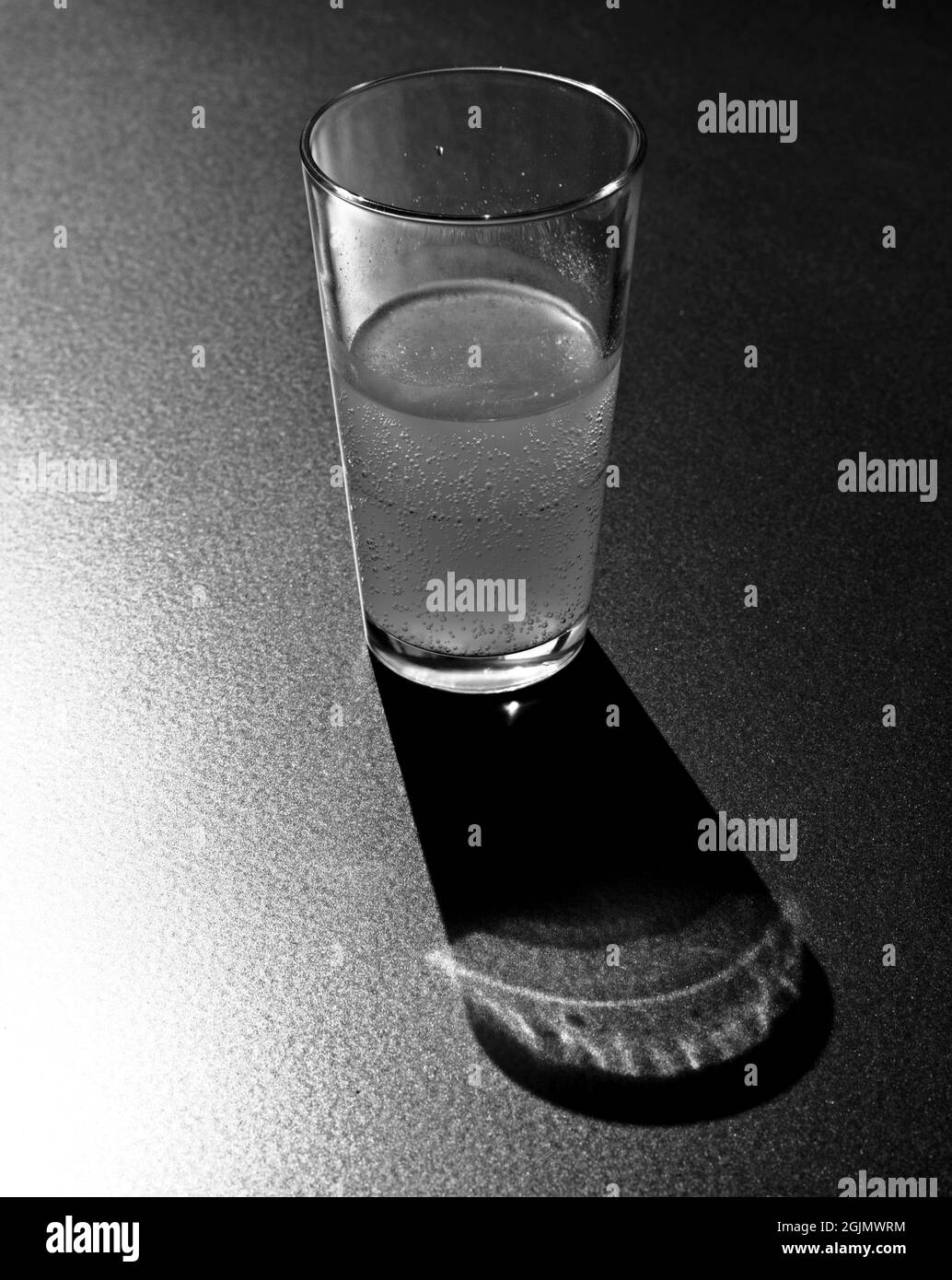 Gros plan en noir et blanc d'un verre avec boisson en contre-jour, avec ombres et reflets au premier plan. Un verre de rafraîchissement. Banque D'Images