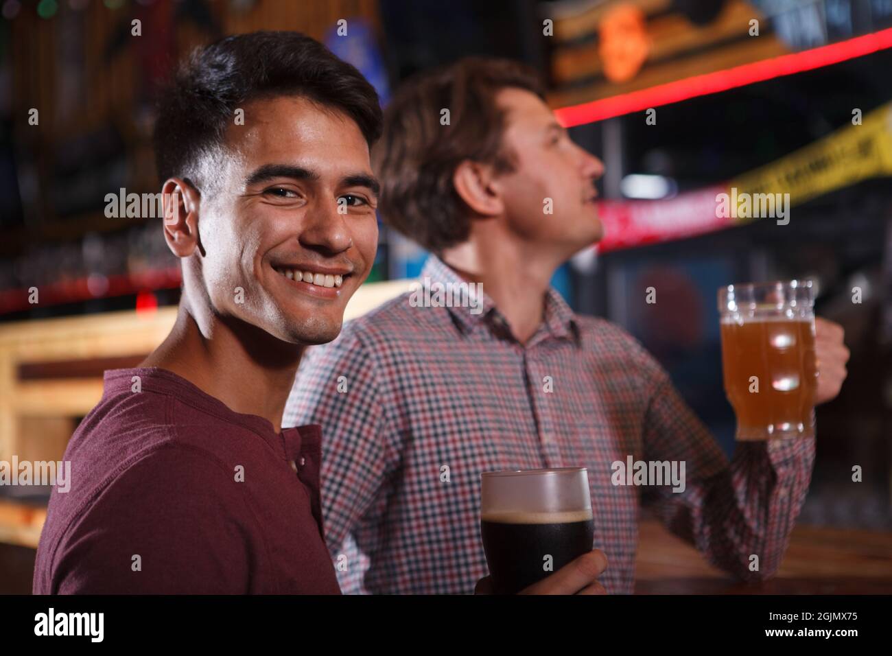 Beau jeune homme souriant à la caméra tout en buvant de la bière avec un ami Banque D'Images
