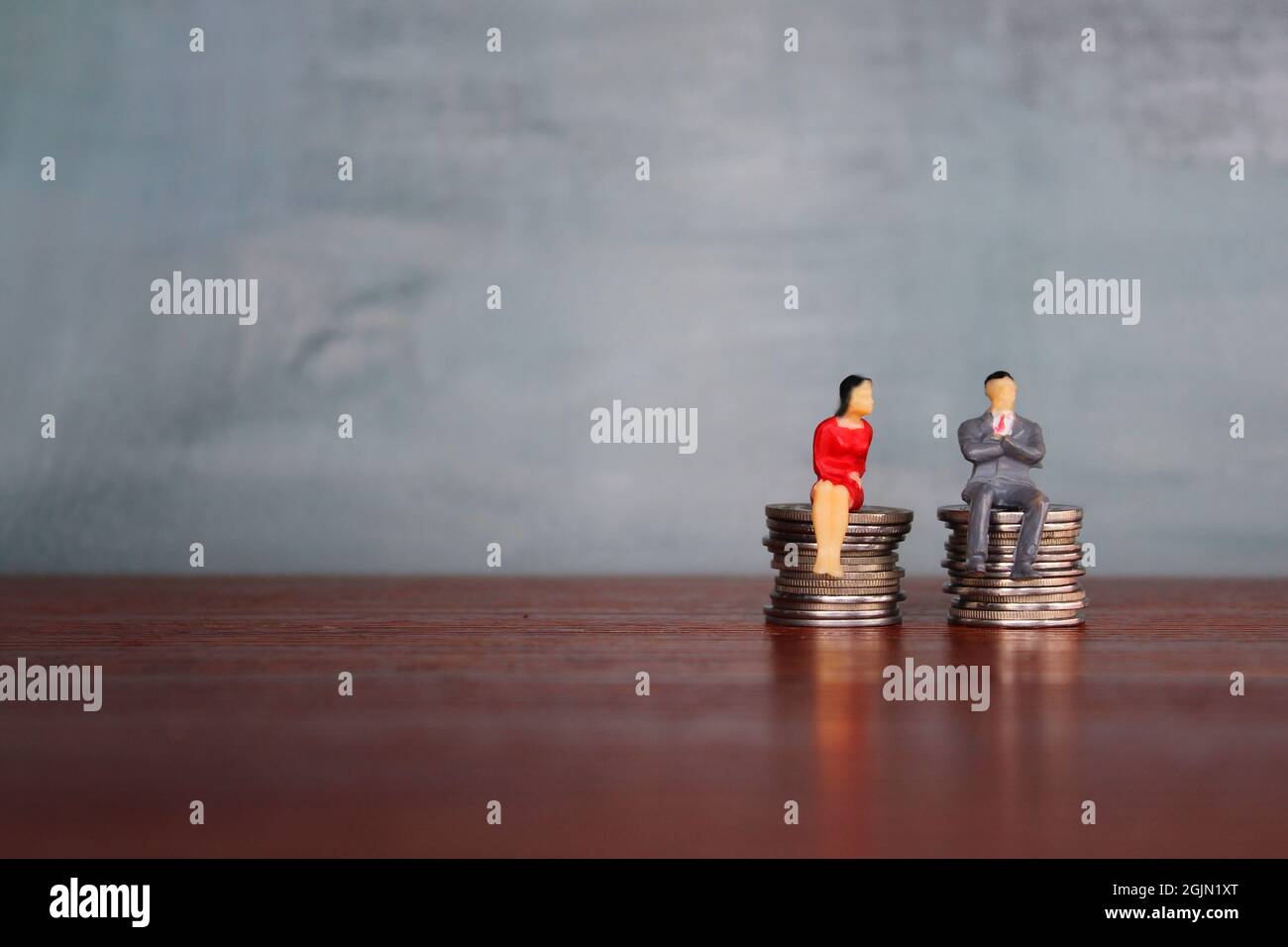 Concept de salaire égal, miniature homme et femme assis sur une pile de pièces de monnaie de même hauteur. Copier l'espace pour le texte Banque D'Images