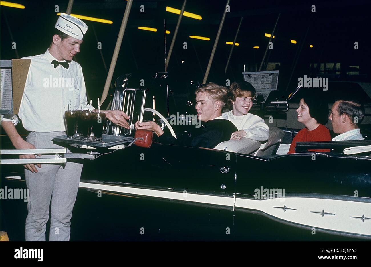 États-Unis dans les années 1960. Deux jeunes couples dans un cabriolet au restaurant Huddle Drive-In 1964. Un serveur reçoit un paiement pour les boissons non alcoolisées. Original KODACHROME. Crédit Roland Palm réf. 6-9-17 Banque D'Images