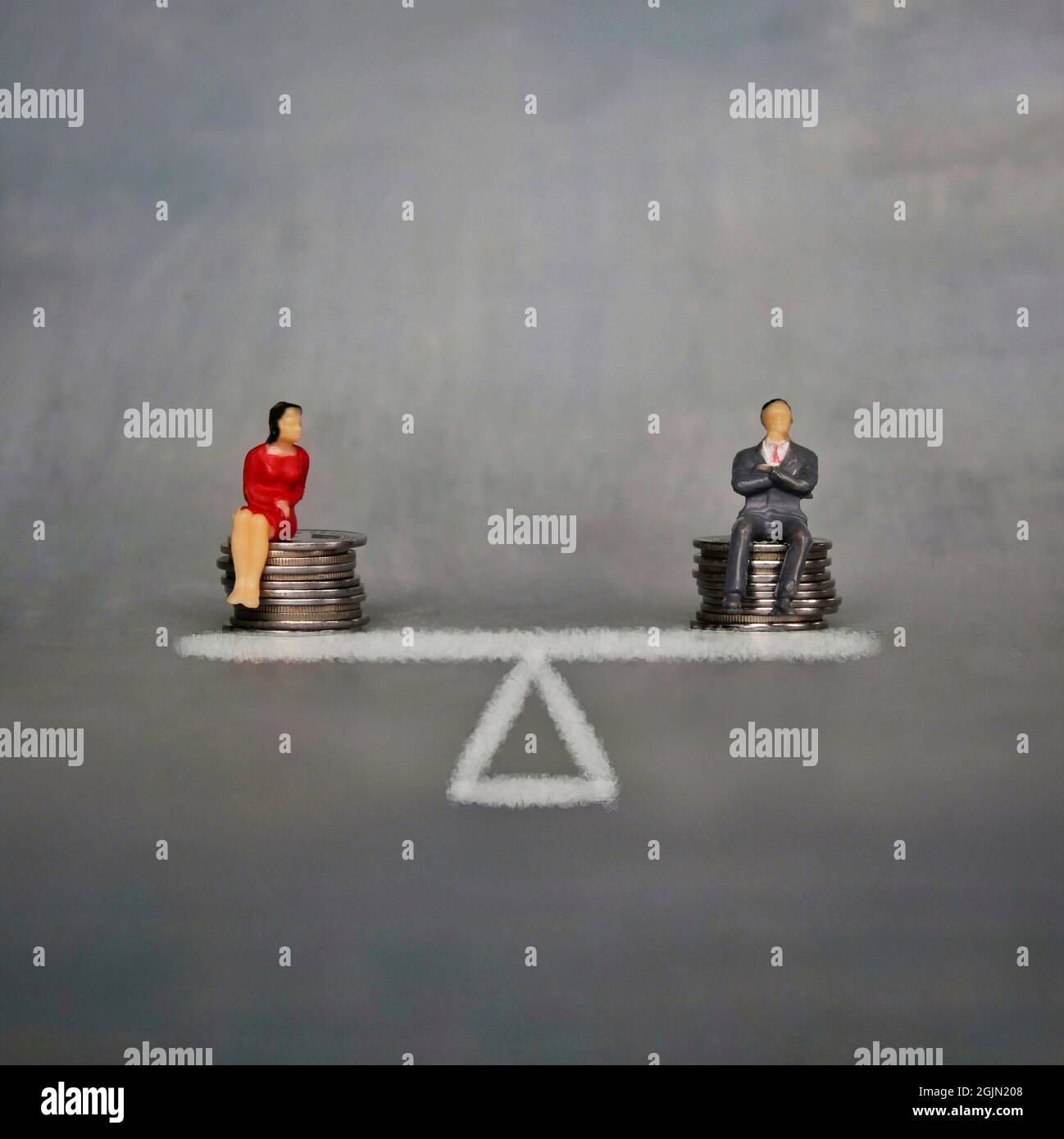 Égalité des sexes et égalité de rémunération. Un homme et une femme miniatures s'assoient sur une pile de pièces et une balance. Banque D'Images