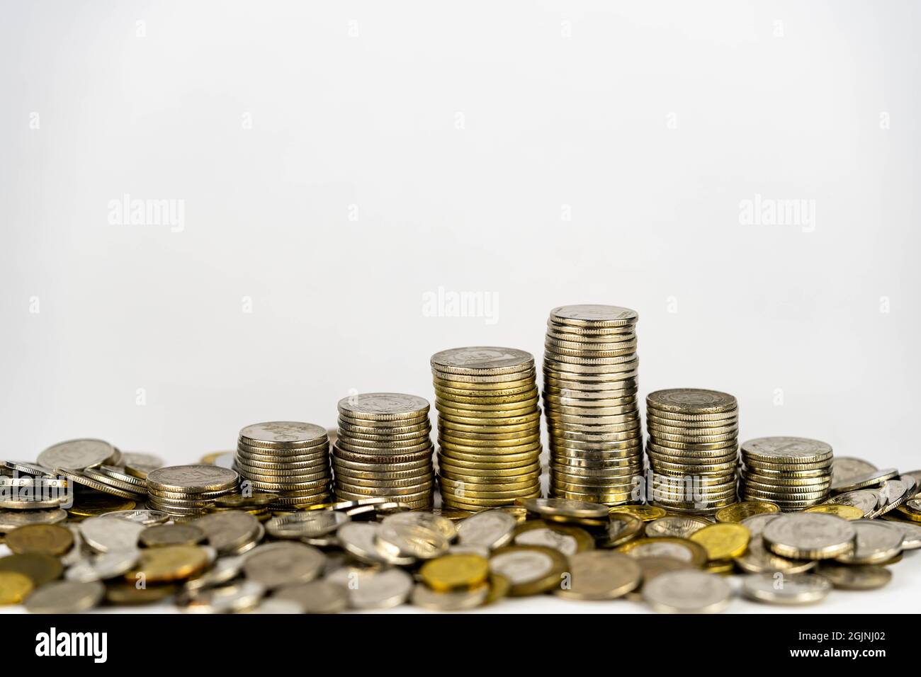 Pièces de monnaie dispersées. Sept piles de pièces dorées de différentes hauteurs disposées dans le sens de la croissance, isolées sur fond blanc. Banque D'Images