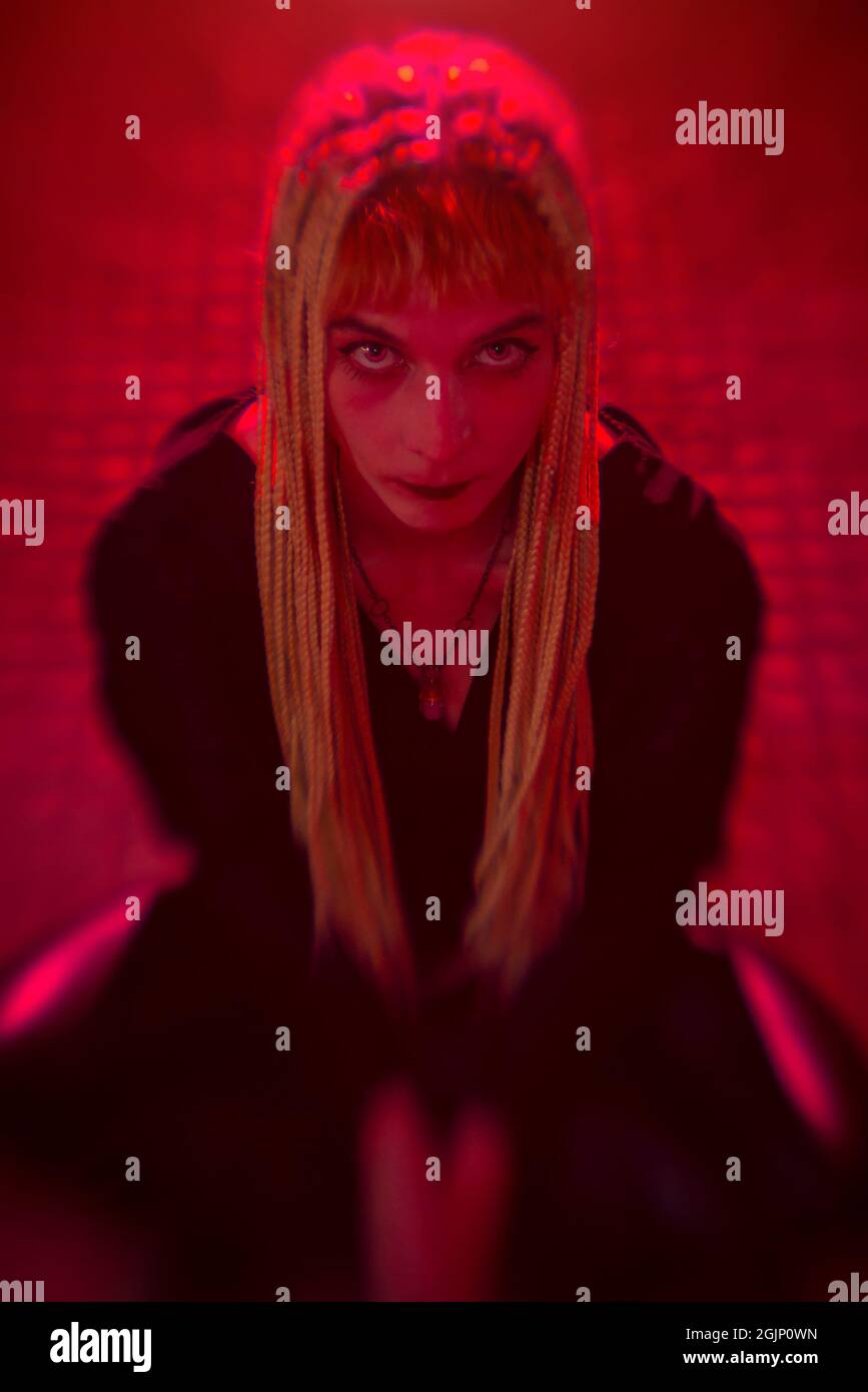 Jeune femme sur ses genoux avec regard diabolat dans ses yeux, lumières rouges, concept d'horreur Banque D'Images