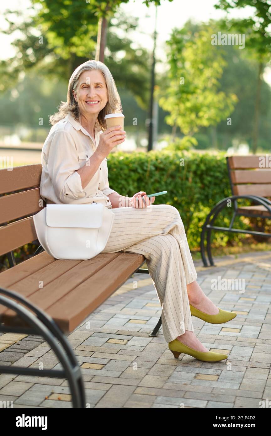 Bonne femme qui a l'air de boire du café sur le banc du parc Banque D'Images