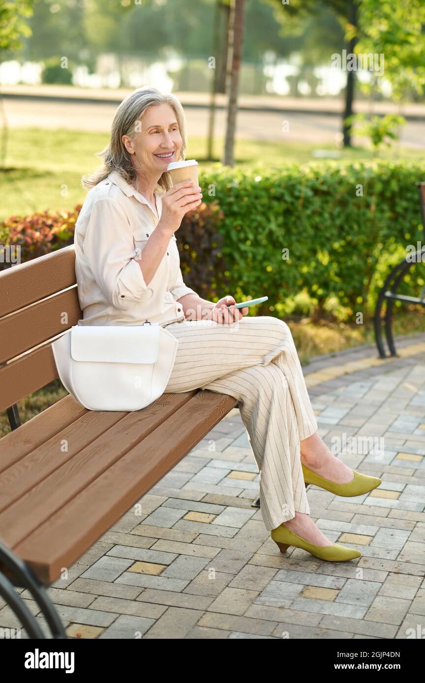 Femme souriante sur le banc du parc avec café Banque D'Images