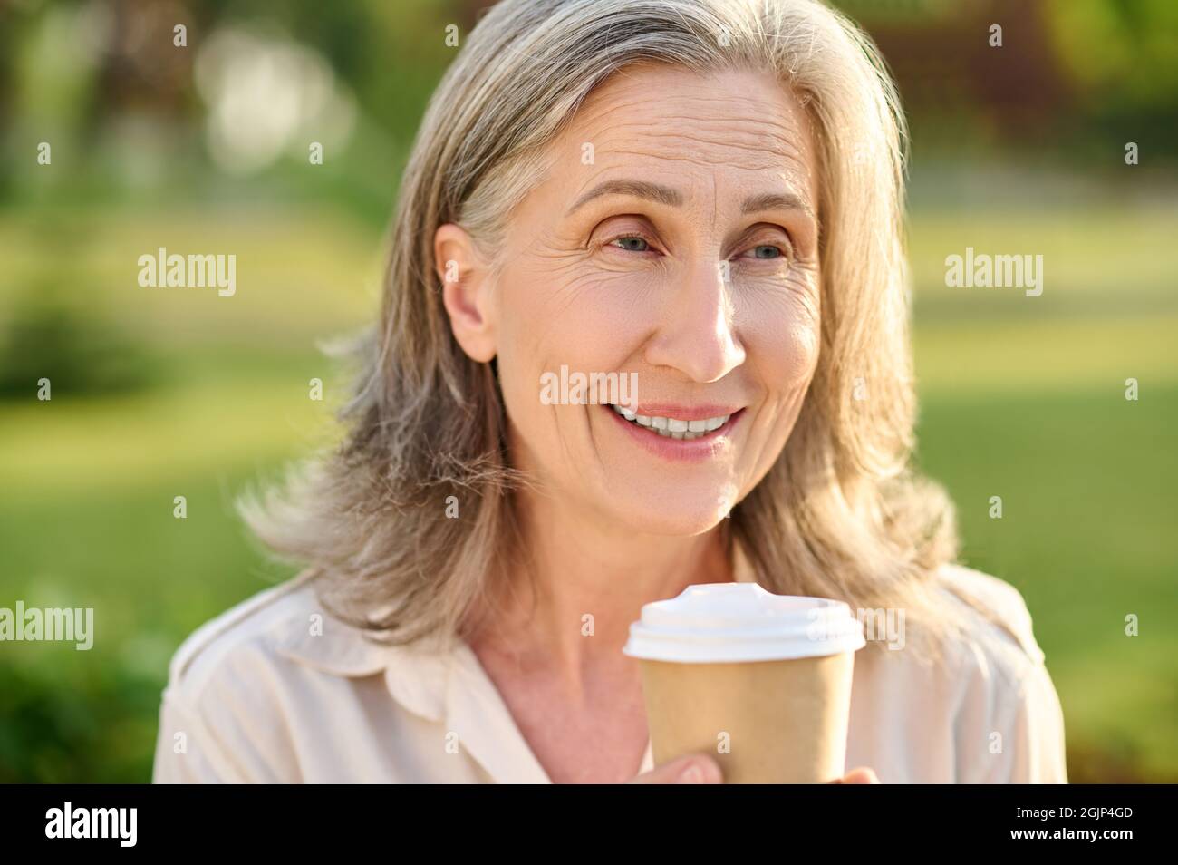 Femme souriante et optimiste avec café à l'extérieur Banque D'Images