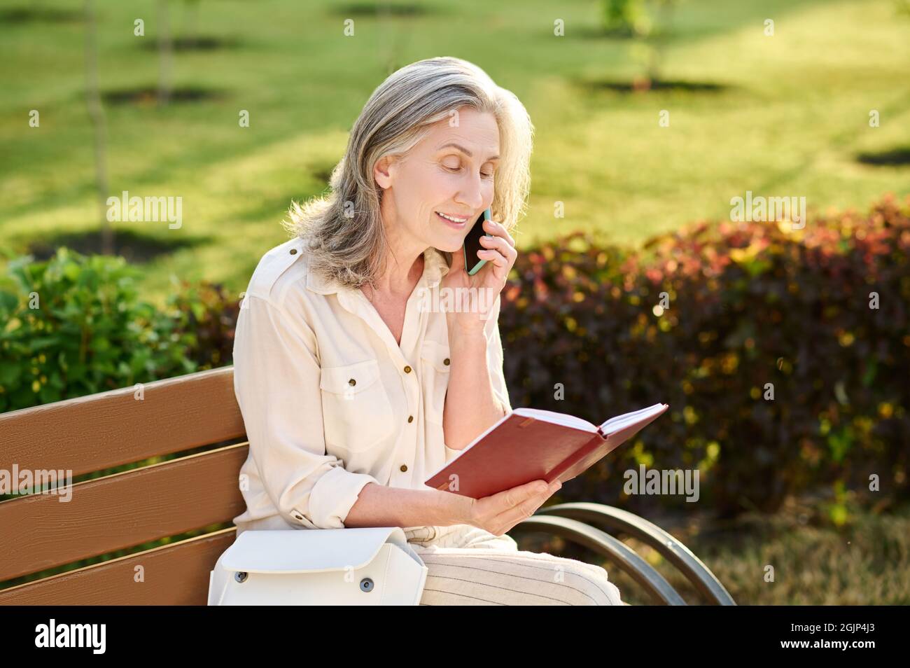 Femme avec un smartphone proche de l'oreille lisant le carnet Banque D'Images