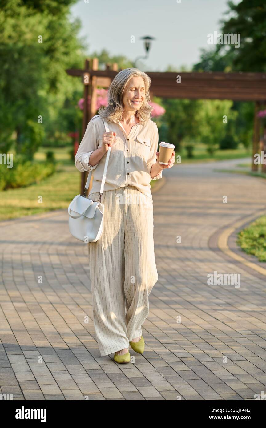 Femme souriante avec un café dans le parc Banque D'Images