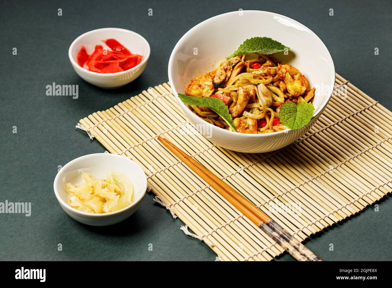 NOUILLES WOK avec fruits de mer et légumes. Moules, crevettes et calmars frits dans l'huile. Délicieux déjeuner asiatique dans un bol blanc sur un tapis de bambou. Remuez le noo Banque D'Images