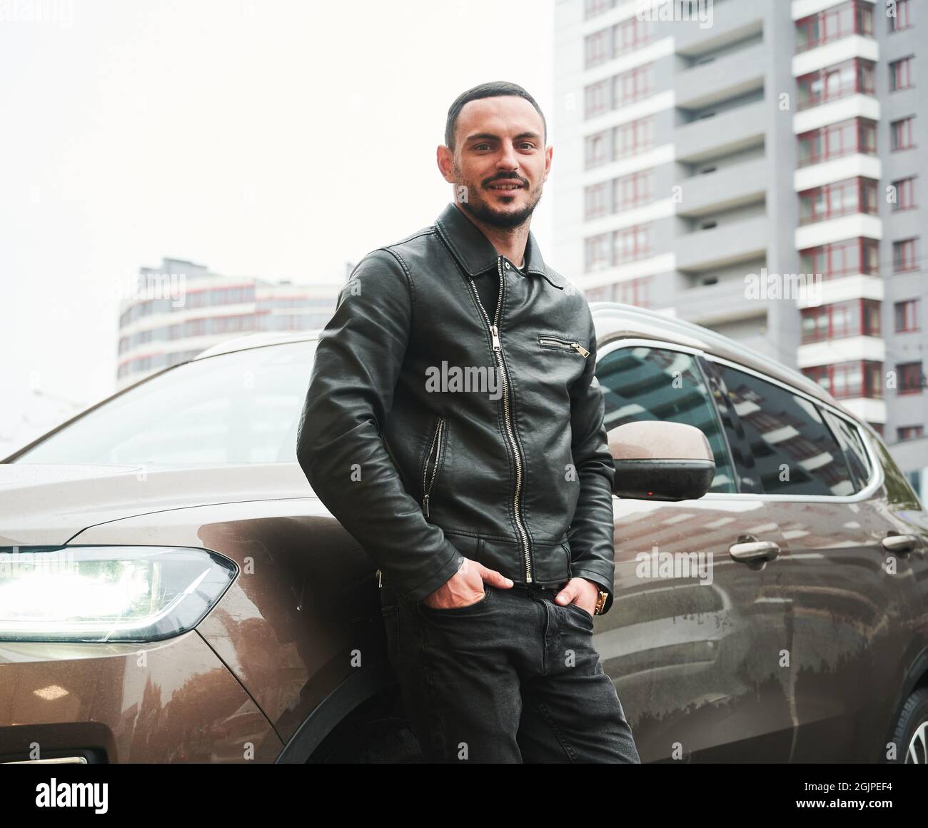 Portrait d'un jeune homme beau posant près de sa voiture moderne à l'extérieur. Banque D'Images