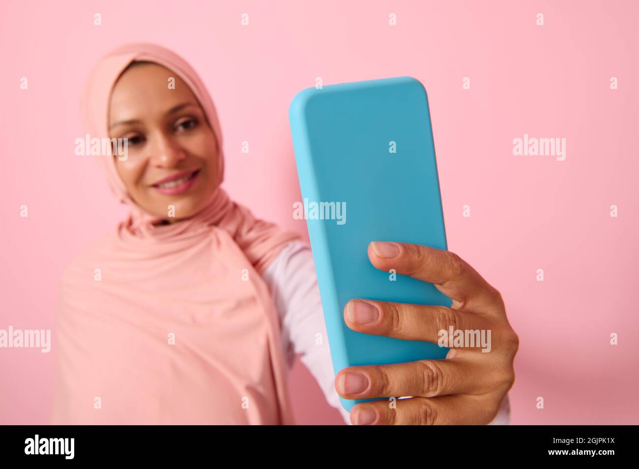 Attention douce portée sur le smartphone dans une couverture bleue dans les bras étendus de la femme arabe musulmane portant la tenue religieuse traditionnelle islamique, hijab rose, et smil Banque D'Images