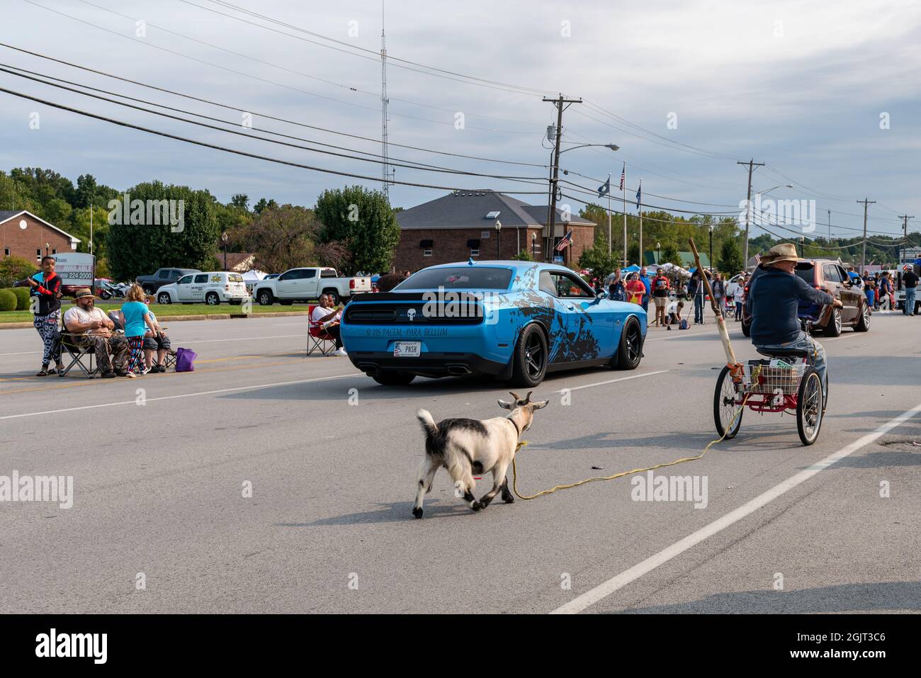 Radcliff, KY, États-Unis, 11 septembre 2021, Un Dodge Challenger bleu descend Lincoln Trail Boulevard pendant qu'un homme roule à vélo le long de la Radcliff Cultural Festival Parade avec une chèvre sur une laisse. Crédit : Brian Koellish/Alamy Live News Banque D'Images