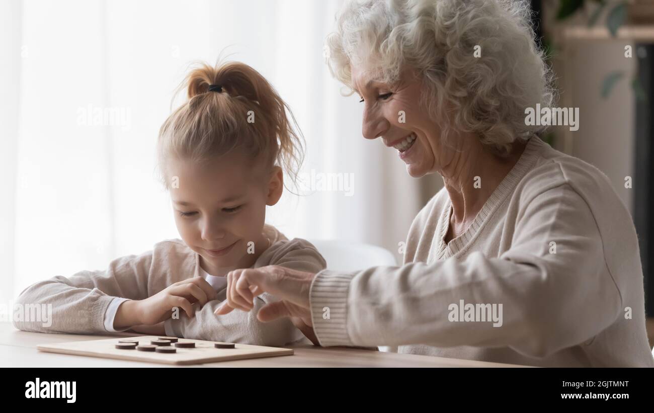 Gai curieux petite fille apprenant à jouer aux dames avec granny. Banque D'Images