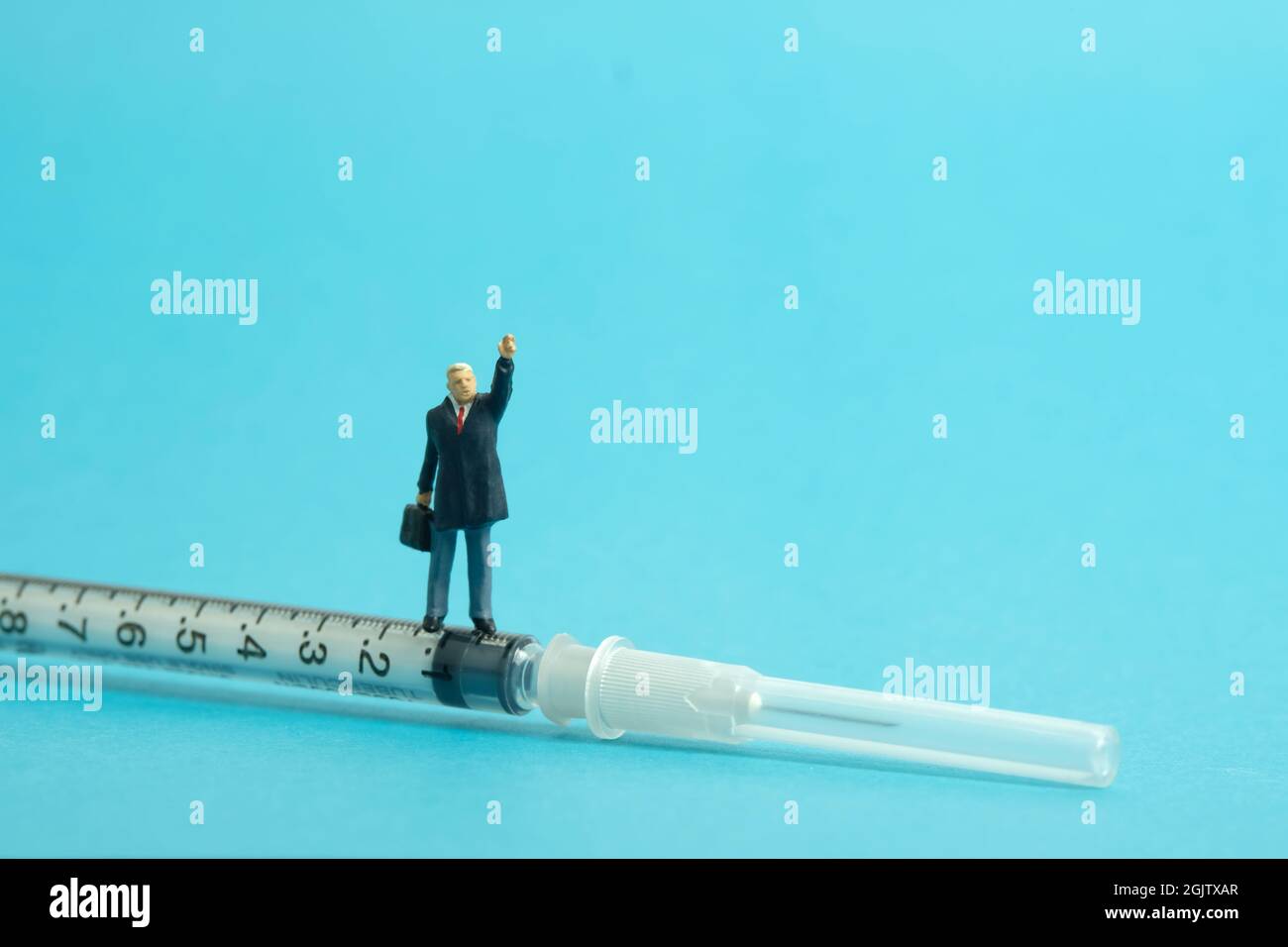 Photographie miniature de personnage de jouet de personnes. Concept d'encouragement à la vaccination. Un homme d'affaires debout au-dessus du vaccin à seringue tout en levez la main. Isoler Banque D'Images