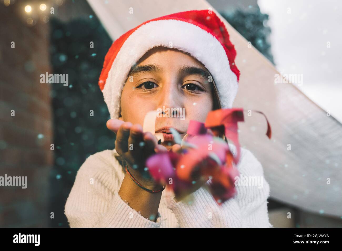 Jeune fille soufflant confetti tout en s'amusant pendant l'heure de Noël - enfant portant chapeau de Santa Clause - Focus sur le visage Banque D'Images