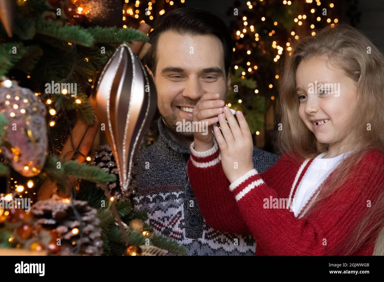 Joyeux jeune père décorant arbre de noël avec petite fille. Banque D'Images