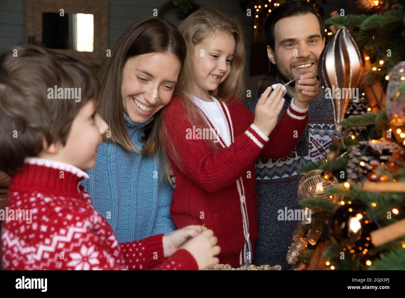 Une famille heureuse et aimante s'implique dans la décoration de Noël arbre à feuilles persistantes festives. Banque D'Images