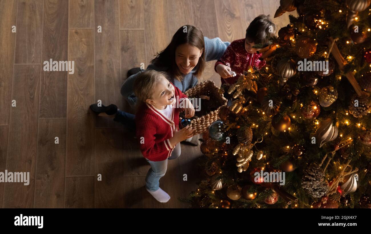 Petite fille adorable décorant arbre de Noël avec maman et frère. Banque D'Images